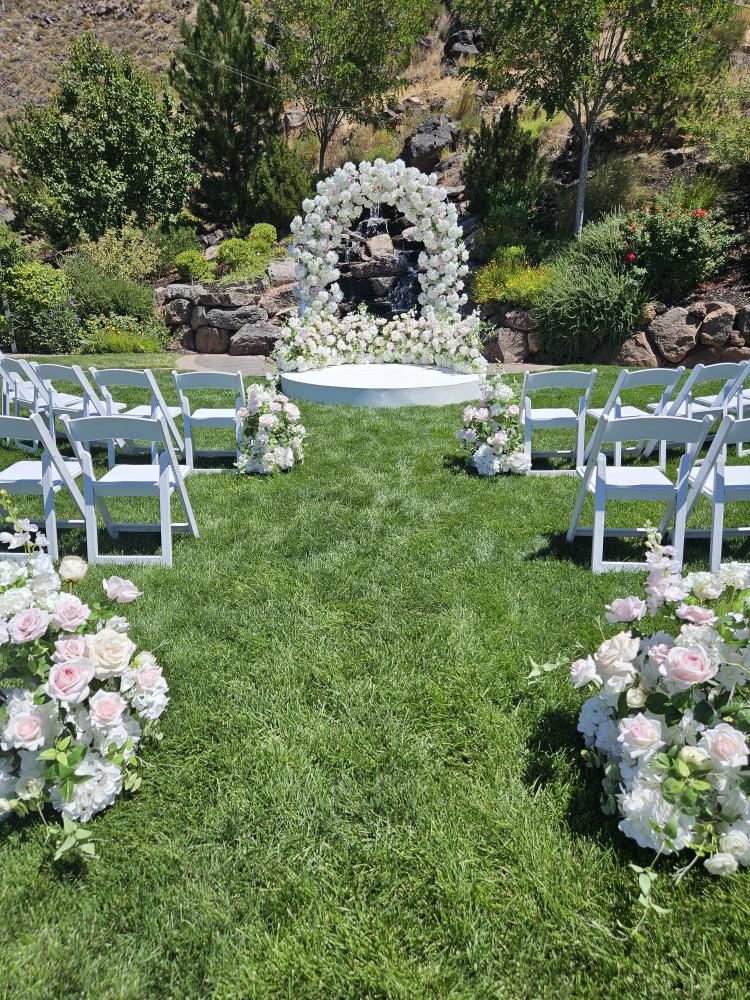 Outdoor wedding ceremony with luxury floral arch, aisle flowers, and platform.