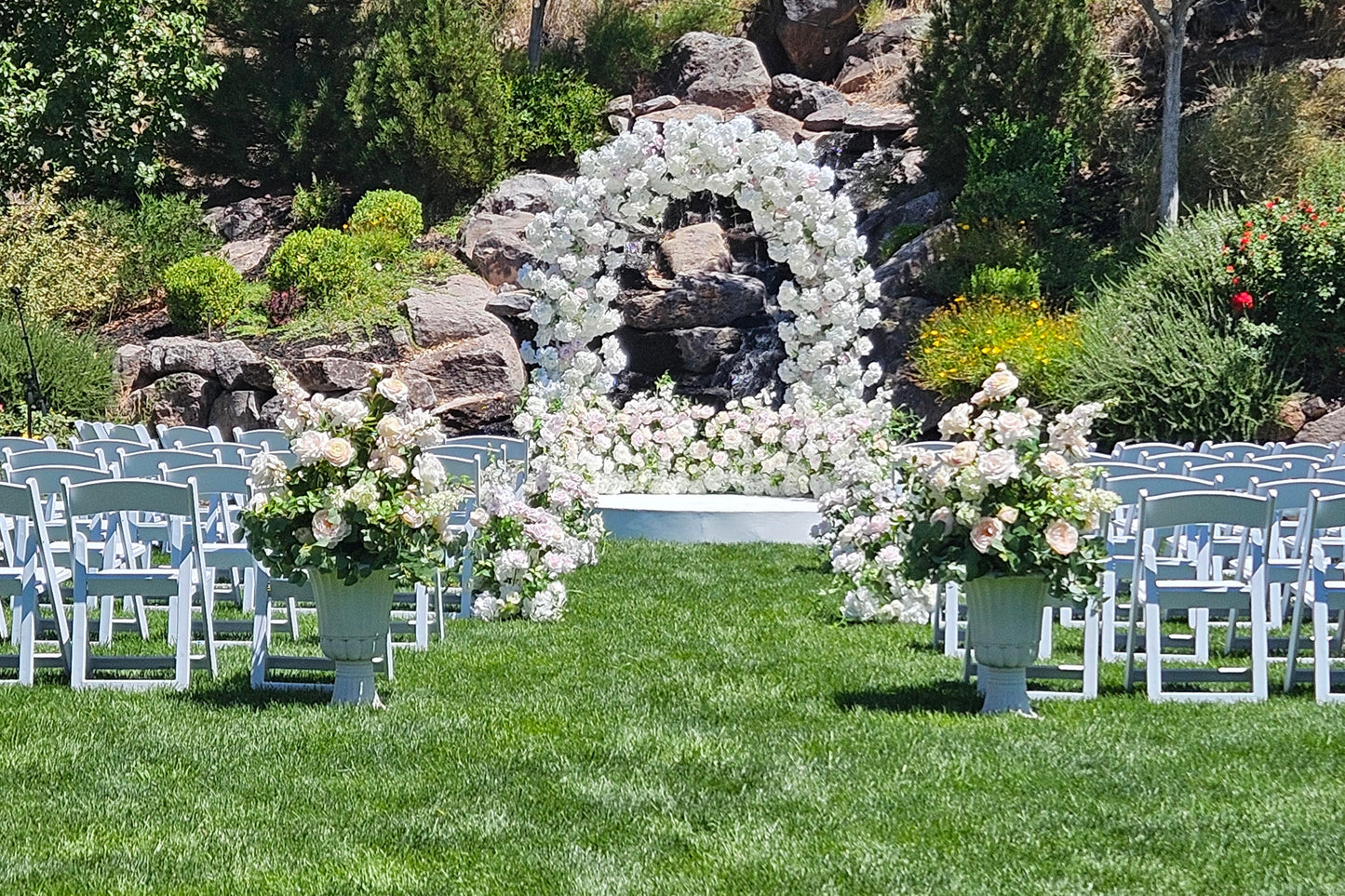 White Wedding ceremony flower arch with aisle flowers and urns on a grassy beautiful venue