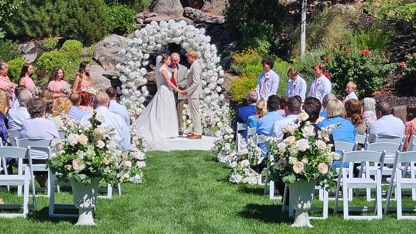 Outdoor wedding ceremony with floral arrangements and guests seated on a grassy field.