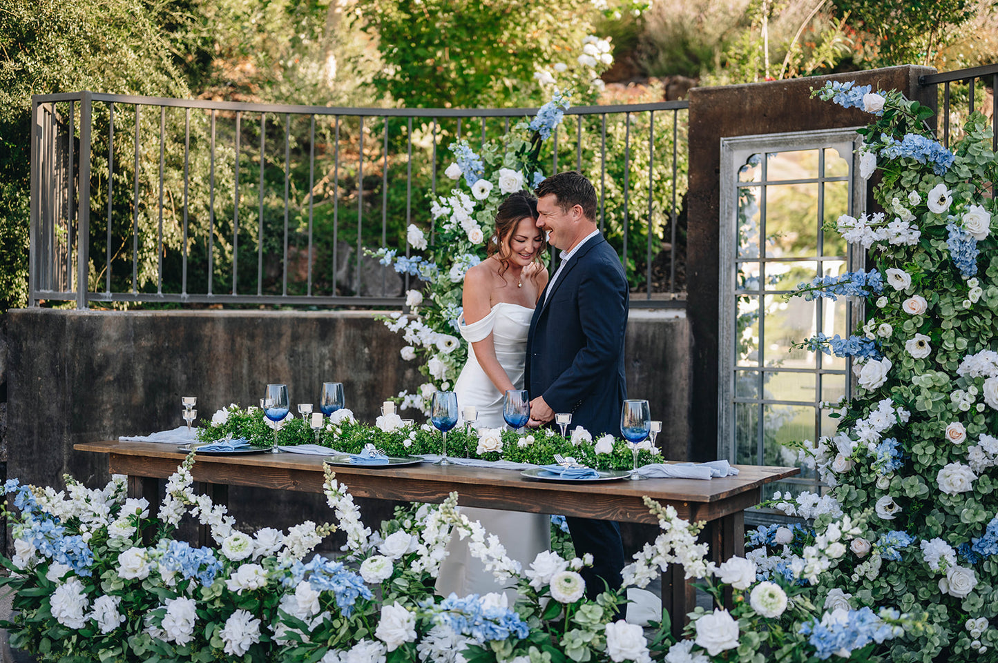 Bride and Groom at Sweetheart table laughing in delight surrounding by white and blue flowers